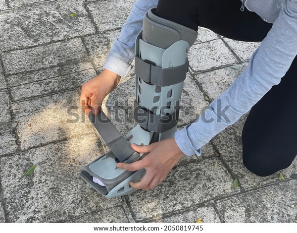 Person bending down in the street adjusting the\
velcro straps of the orthopedic walking boot, ideal for people with\
leg injuries such as tibia or fibula fracture. Patient walking down\
the street.
