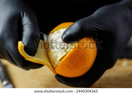 Person with black gloves peeling full orange on wooden cutting board. High quality photo