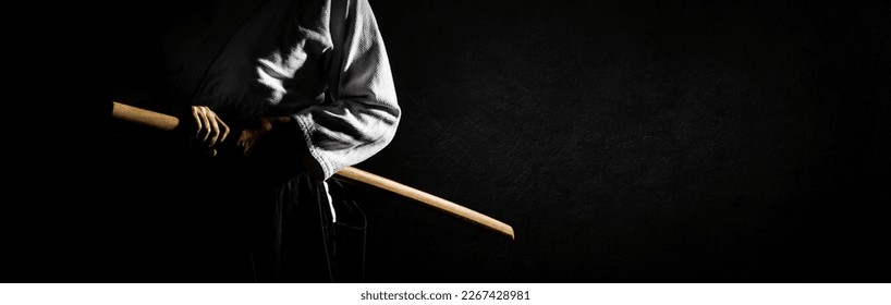 A person in black hakama standing in fighting pose with wooden sword bokken over grunge dark background banner. Shallow depth of field. SDF.  - Powered by Shutterstock