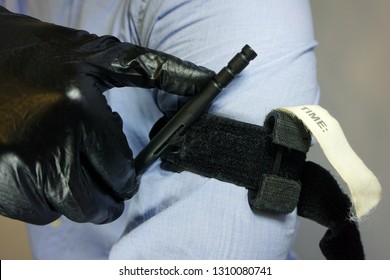 Person in black medical gloves Applies the tourniquet to his hand to prevent bleeding during the first aid. Trauma patient. Combat tactical Equipment. Combat Application Tourniquet                    