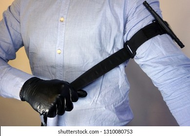  Person in black medical gloves Applies the tourniquet to his hand to prevent bleeding during the first aid. Trauma patient. Combat tactical Equipment. Combat Application Tourniquet                   