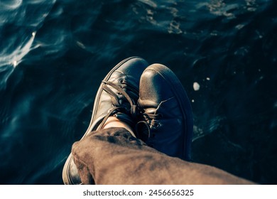 Person with black shoes dangling feet over water, capturing a moment of calm and reflection. High quality photo - Powered by Shutterstock