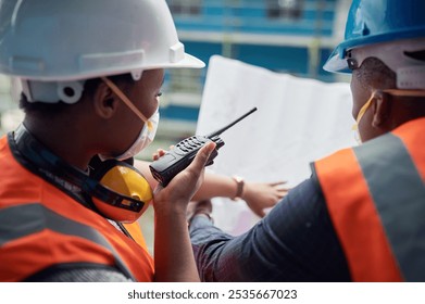 Person, blueprint and radio with construction, inspection and builder floor plan with collaboration. Industrial, face mask and conversation with project management and property assessment for safety - Powered by Shutterstock