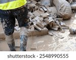 Person in boots standing on a muddy site with debris after a flood in Valencia, Spain