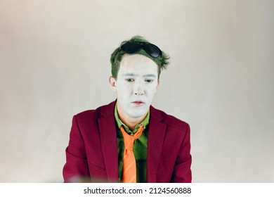 Person In Bordo Suit, Shirt With Yellow Stripes Tie Looks Down. Actor With White Makeup On Face, Color Eyes And Green Hair. Paint Of Clown Or Mime. Theater Concept. Black Glasses On Head.