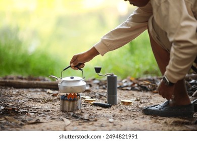 A person brewing coffee outdoors using a portable stove, kettle, and manual coffee grinder. The serene natural setting enhances the experience of making and enjoying coffee in the wild.  - Powered by Shutterstock