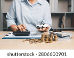 Person calculating auto financing while holding a white toy car, with calculator, cash, and coins on desk, representing car loan budgeting, vehicle purchase cost, and finance management.