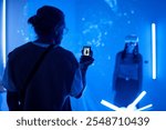 Person capturing immersive virtual reality experience with smartphone, highlighting interaction with technology in blue-illuminated environment