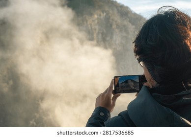 Person capturing scenic mountain view with smartphone in misty landscape