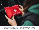 A person is carefully holding a bright red first aid kit securely inside a car, emphasizing the crucial importance of being prepared for emergencies while traveling on the road