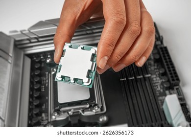 A person is carefully holding a computer processor above a motherboard socket, preparing to install it.