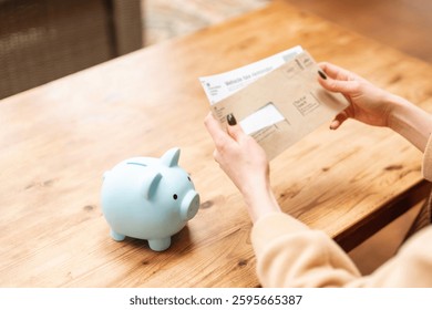 Person checks mail while preparing to save money with a piggy bank on a wooden table at home on a sunny day