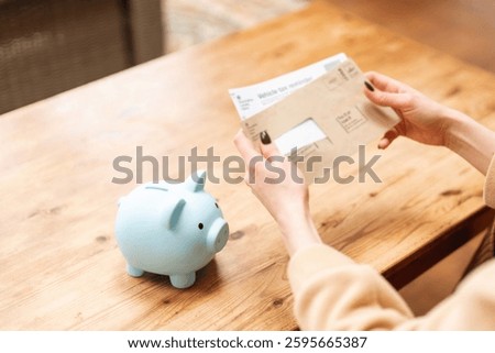 Person checks mail while preparing to save money with a piggy bank on a wooden table at home on a sunny day