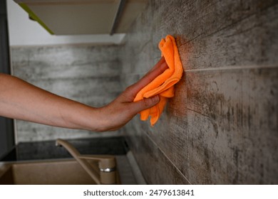 Person is cleaning kitchen wall tiles using orange microfiber cloth. - Powered by Shutterstock