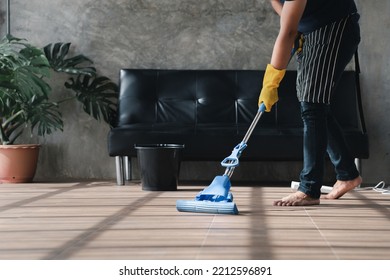 Person Cleaning The Room, The Cleaning Worker Is Using A Mop To Clean The Floor Of The Living Room In The Company Office. Cleaning Staff. Maintaining Cleanliness In The Organization.