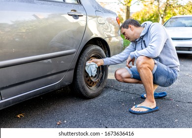 Person Cleaning Tire Wheel With Missing Cap Cover On Parked Car With Man Rubbing Rusty Hubcap With Towel