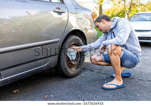 Person cleaning tire\
wheel with missing cap cover on parked car with man rubbing rusty\
hubcap with towel