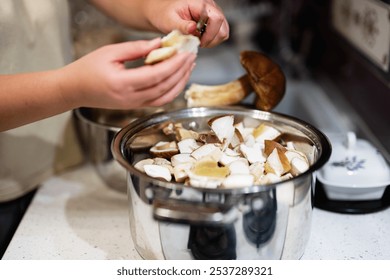 A person cleans and chops fresh mushrooms, placing them into a pot in a modern kitchen setting, emphasizing home cooking and culinary preparation. - Powered by Shutterstock