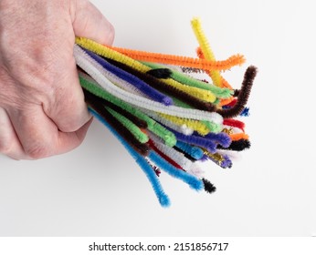Person Clutching A Bunch Of Sparkle And Neon Rainbow Pipe Cleaners On A White Background