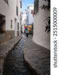 Person with a colorful umbrella walking along a narrow stone path with a stream in a white building alley, Alpujarras, granada, andalucia, espa a