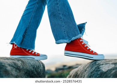 A person confidently walks on rocky terrain wearing vibrant red sneakers and stylish blue flared jeans - Powered by Shutterstock