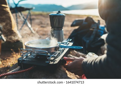 person cooking in nature camping outdoor, cooker prepare breakfast picnic on metal gas stove, hot tea outside; campsite lifestyle - Powered by Shutterstock