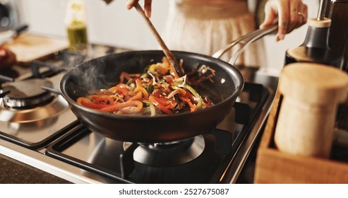 Person, cooking and pan with stir fry on stove for food, meal prep or vegetables in kitchen at home. Closeup, spoon and wok with peppers and organic ingredients for taste, diet or lunch at house - Powered by Shutterstock