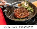 A person is cooking a tenderloin steak in a pan with herbs and spices. The steak is brown and he is well-cooked