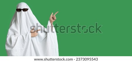 Person in costume of ghost pointing at something on green background with space for text. Halloween celebration
