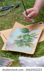 A person is currently engaged in the creative process of painting a detailed picture of a plant on a piece of white paper