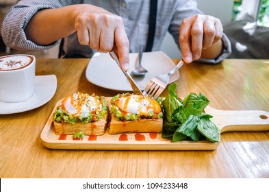 A Person Cutting Eggs Benedict With Avocado And Hot Sauce