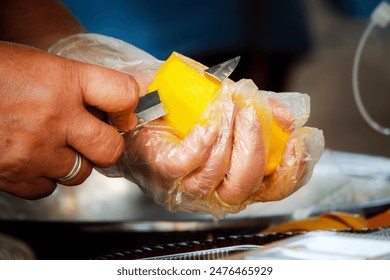 A person is cutting a mango with a knife. The knife is in the person's hand and the mango is on a plate - Powered by Shutterstock