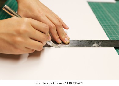 Person Cutting White Foam Board Paper With An Exacto Knife And Measuring With Metal Ruler 