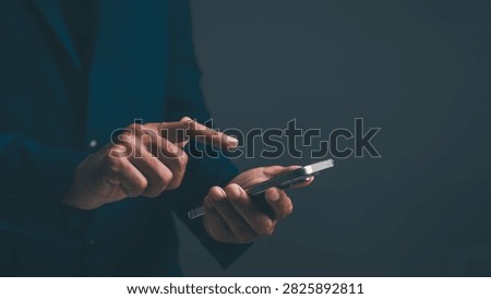 A person in a dark suit using a smartphone against a dark background, focusing on hand interaction with the device.