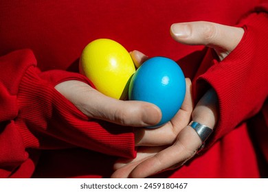 A person delicately holds two colorful Easter eggs in their hands, showcasing the vibrant hues and intricate designs. - Powered by Shutterstock