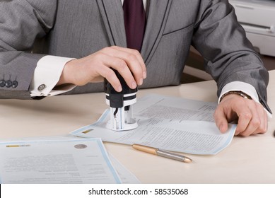 A Person At A Desk Using A Stamp Or Corporate Seal On Documents