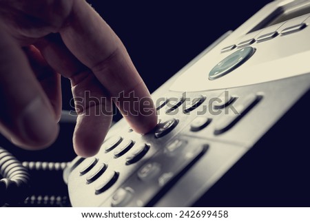 Person dialing out on a telephone punching in the numbers on the keypad with a finger, vintage effect toned image.