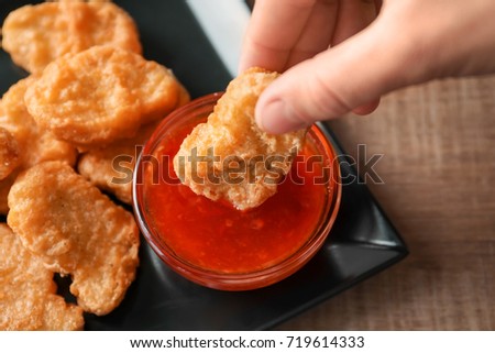 Person dipping chicken nugget in chili sauce indoors