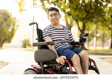 A person with a disability sits in a wheelchair at an outdoor park at sunset.The adult man is smiling at the camera happily.Disabled people in wheelchairs concept. - Powered by Shutterstock