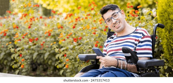 A person with a disability sits in a wheelchair at an outdoor park at sunset.The adult man looks at the camera happily while holding a mobile phone.Disabled people in wheelchairs concept. - Powered by Shutterstock