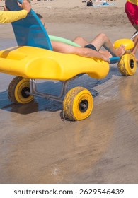 Las personas con discapacidad que usan silla de ruedas en la playa están en una playa accesible. Están rodando hacia el agua, rodeados de arena y otros bañistas en un día soleado.