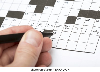 A Person Is Doing A Crossword Puzzle. It Is A Good Training For Brains Specially For Elderly People. The Word Dementia Is Written On The Crossword Puzzle. Focus Point On The Pen Tip.