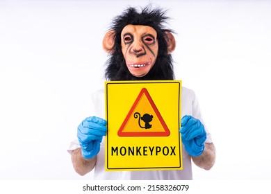 Person dressed in a monkey mask, in a medical nurse's suit, holding a sign with the danger sign and a monkey, which reads: MONKEYPOX, on a white background. Virus, epidemic, Nigeria and smallpox.