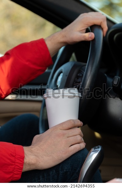 Person driving a car with\
coffee cup.