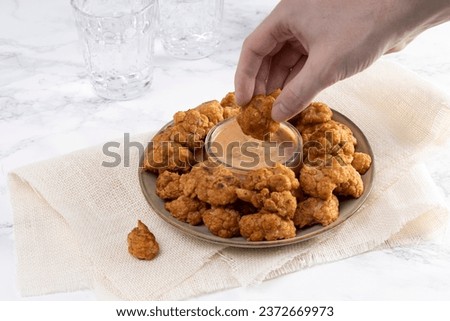 Person eating American-style cauliflower wings with a dill sauce. Vegan and vegetarian diet recipe concept.