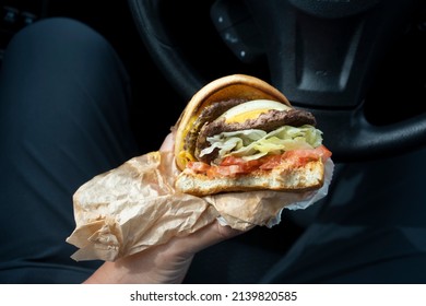 A person eats a double patty cheeseburger ordered from a drive-through burger chain restaurant in his car. Dangerous forever chemicals are said to be found in wrappers at major fast food restaurants. - Shutterstock ID 2139820585