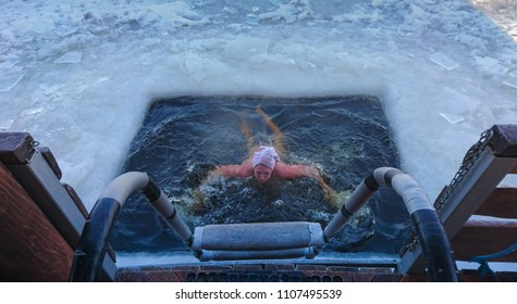 Person Emerging From A Swimming Hole Cut In The Frozen Ice Surface Of A Lake Viewed From The Top Of The Exit Steps