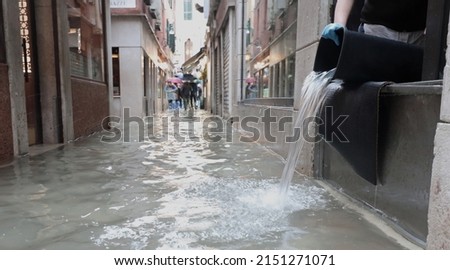 person empties the bucket of water from inside the flooded shop in the alley of Venice in Italy during high tide