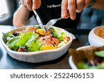 person enjoying a colorful salad with fresh vegetables and meat, using a fork and knife. The focus is on the vibrant, healthy meal, highlighting a theme of nutritious eating and a balanced lifestyle.