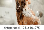 A person enjoying a soothing shower, applying shampoo and surrounded by bubbles in a bright bathroom.